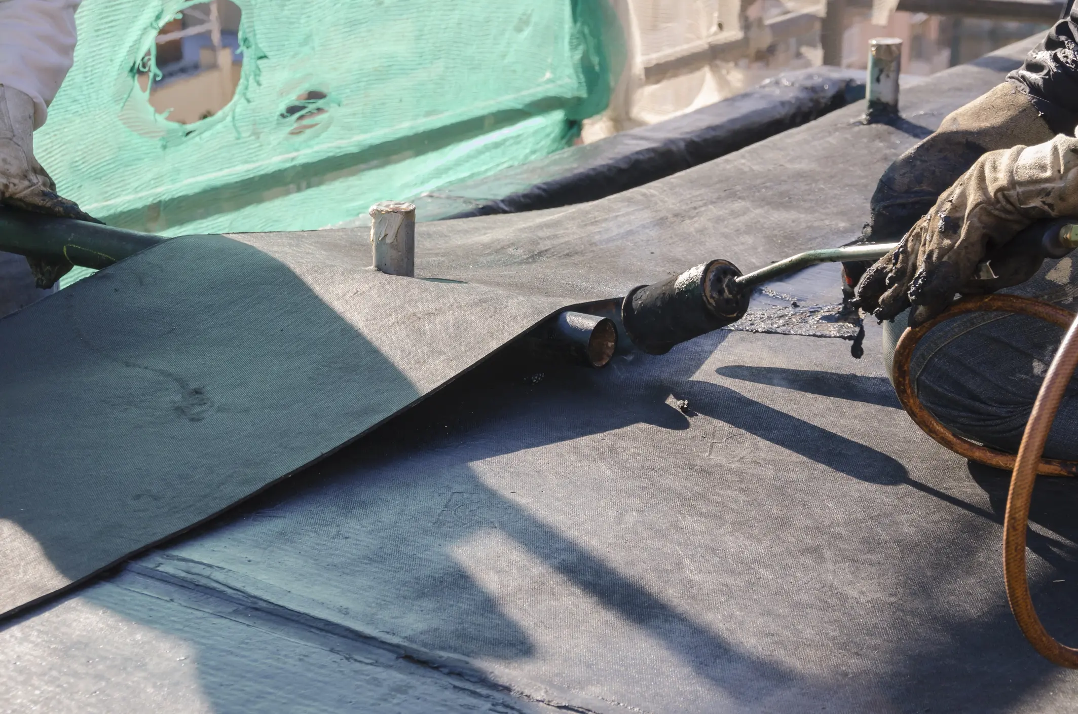 Construction workers sealing roof with tar sheet