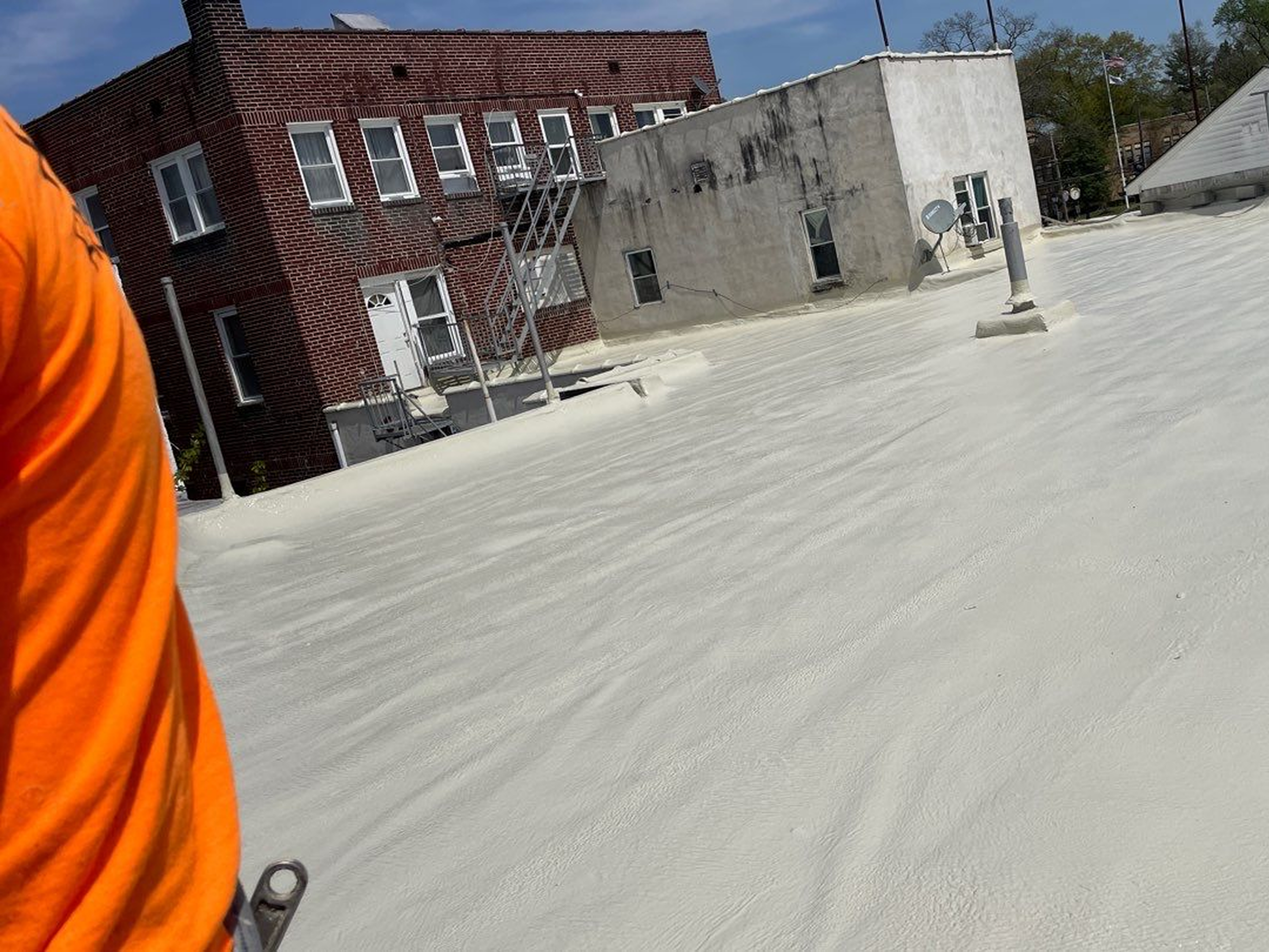 Rooftop with freshly applied white waterproof coating under a clear blue sky.