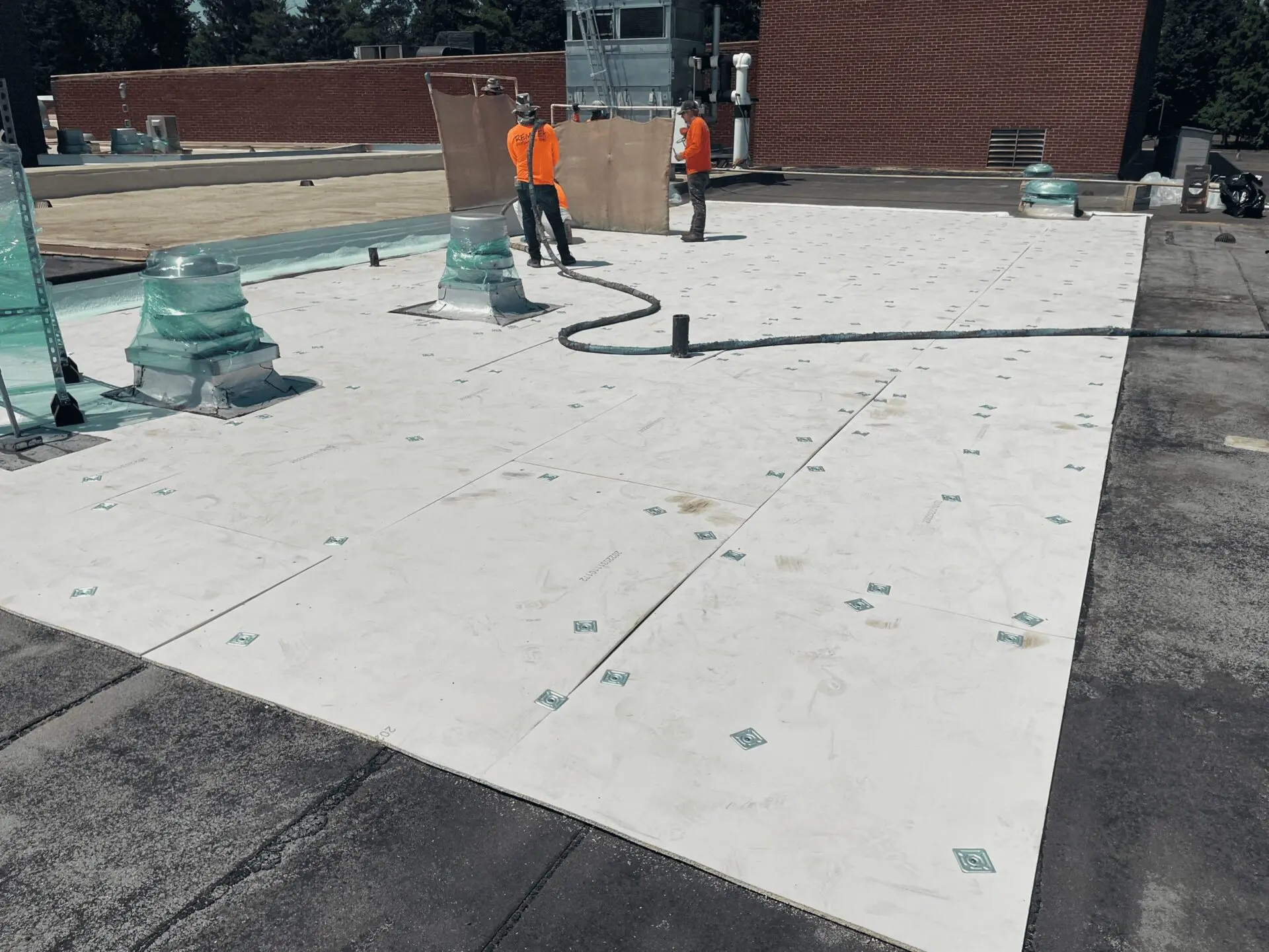 Workers installing a white roofing membrane on a flat roof.
