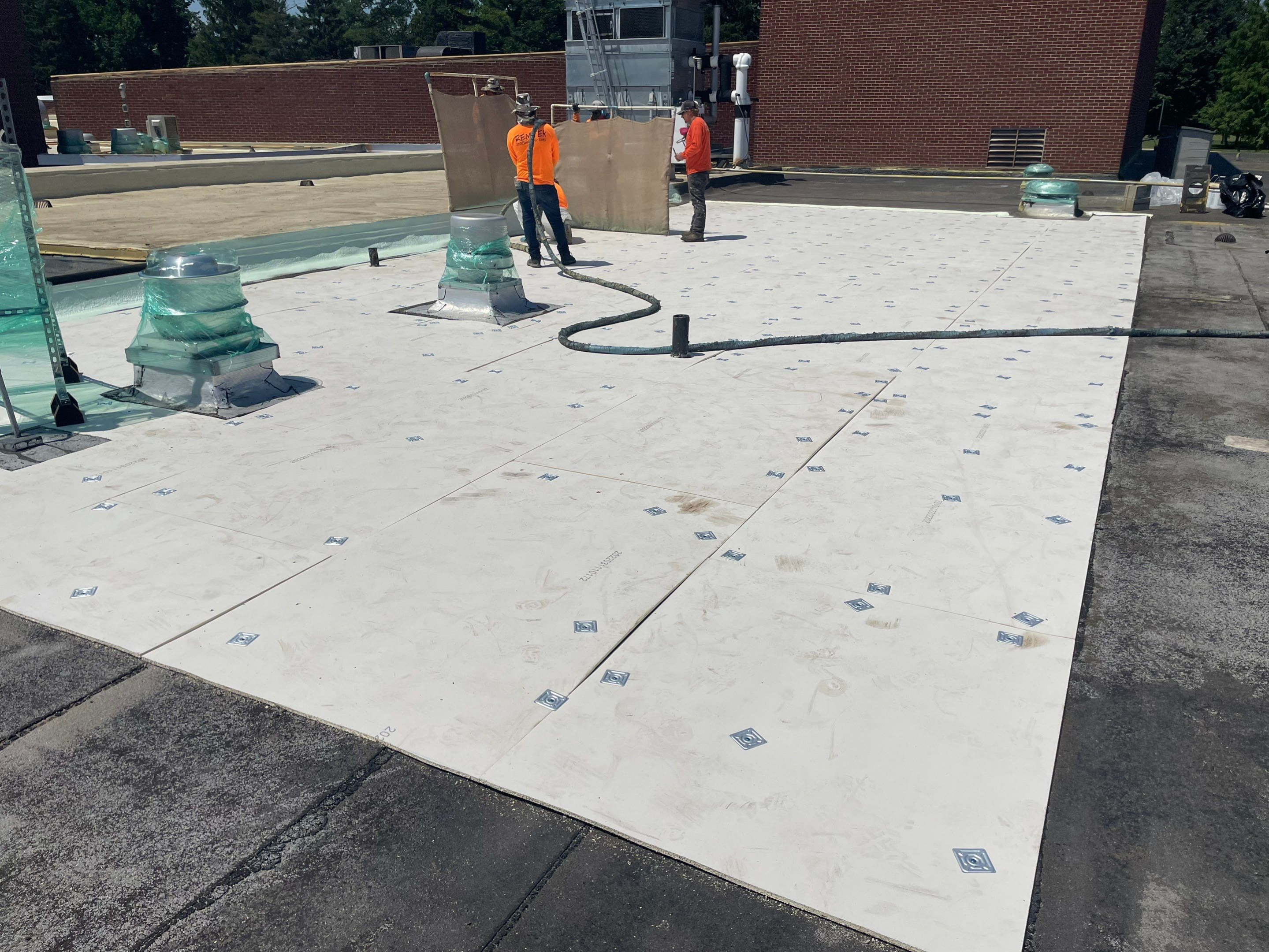 Workers installing a white roofing membrane on a flat roof.