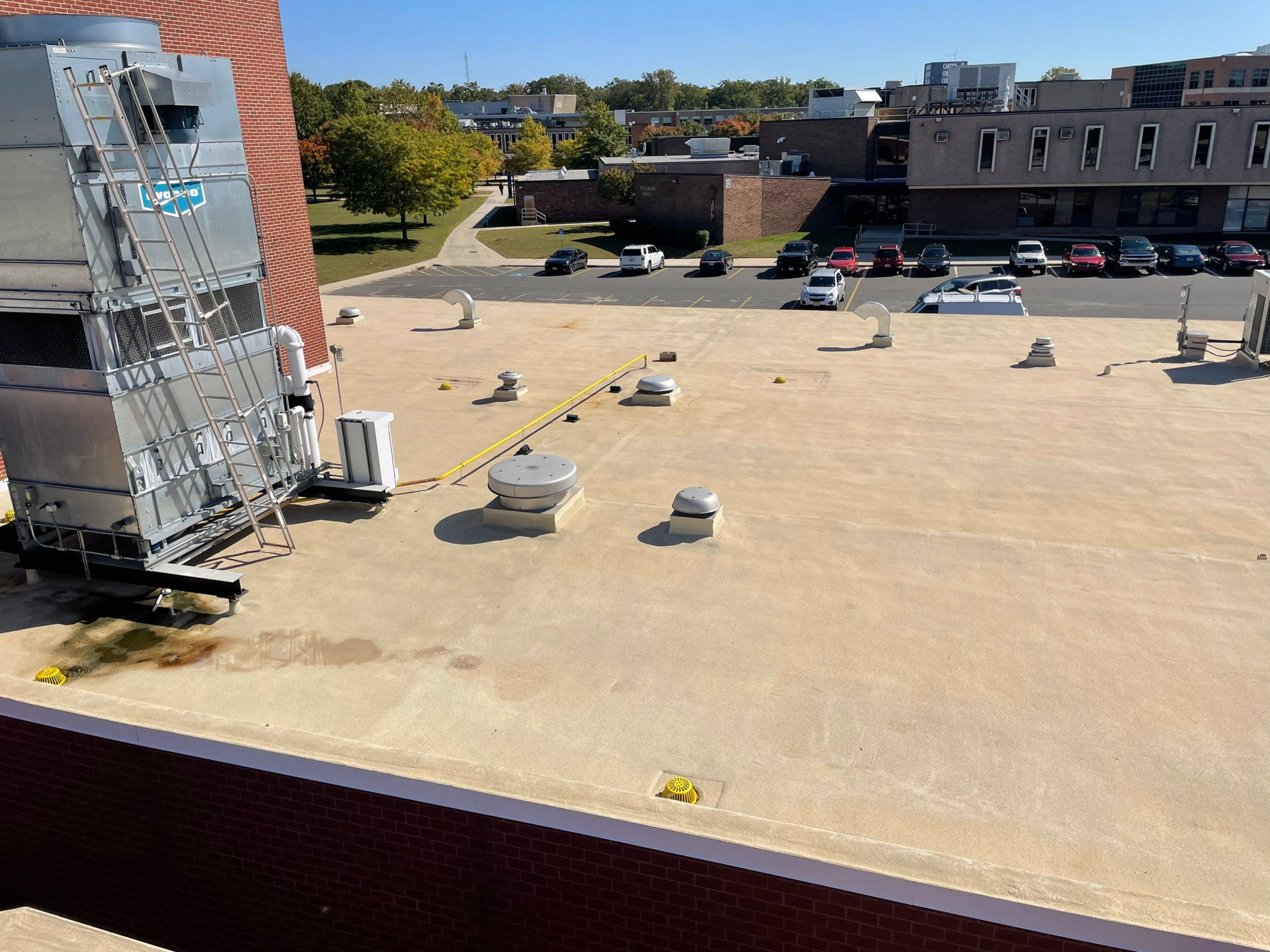 Flat rooftop with ventilation units and parked cars in the background.
