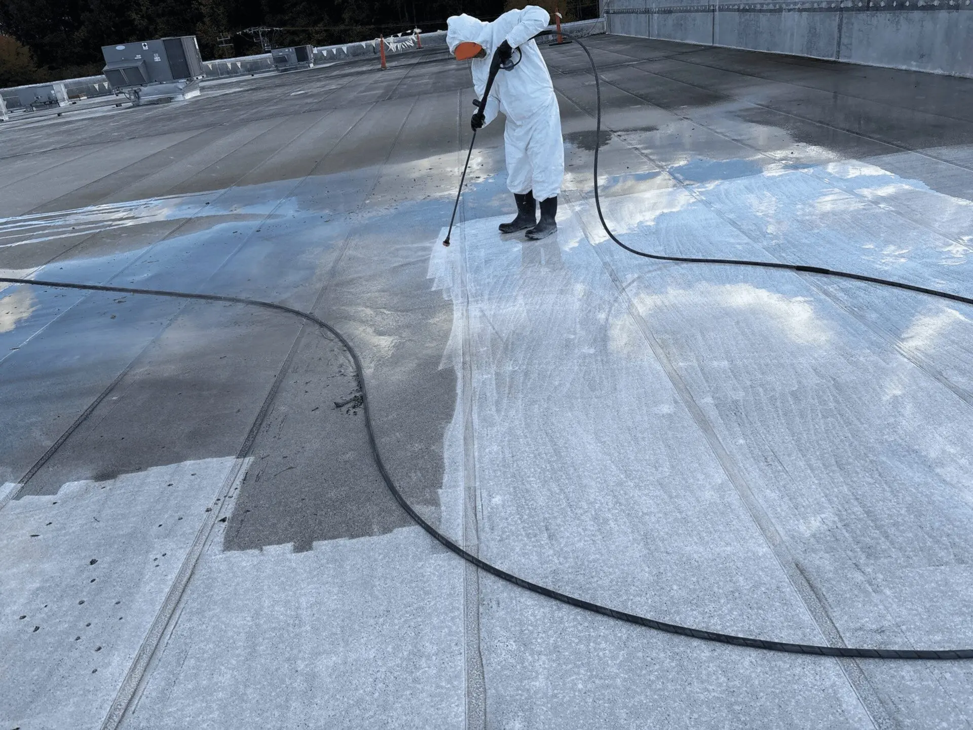 Person pressure washing a large concrete surface outdoors.