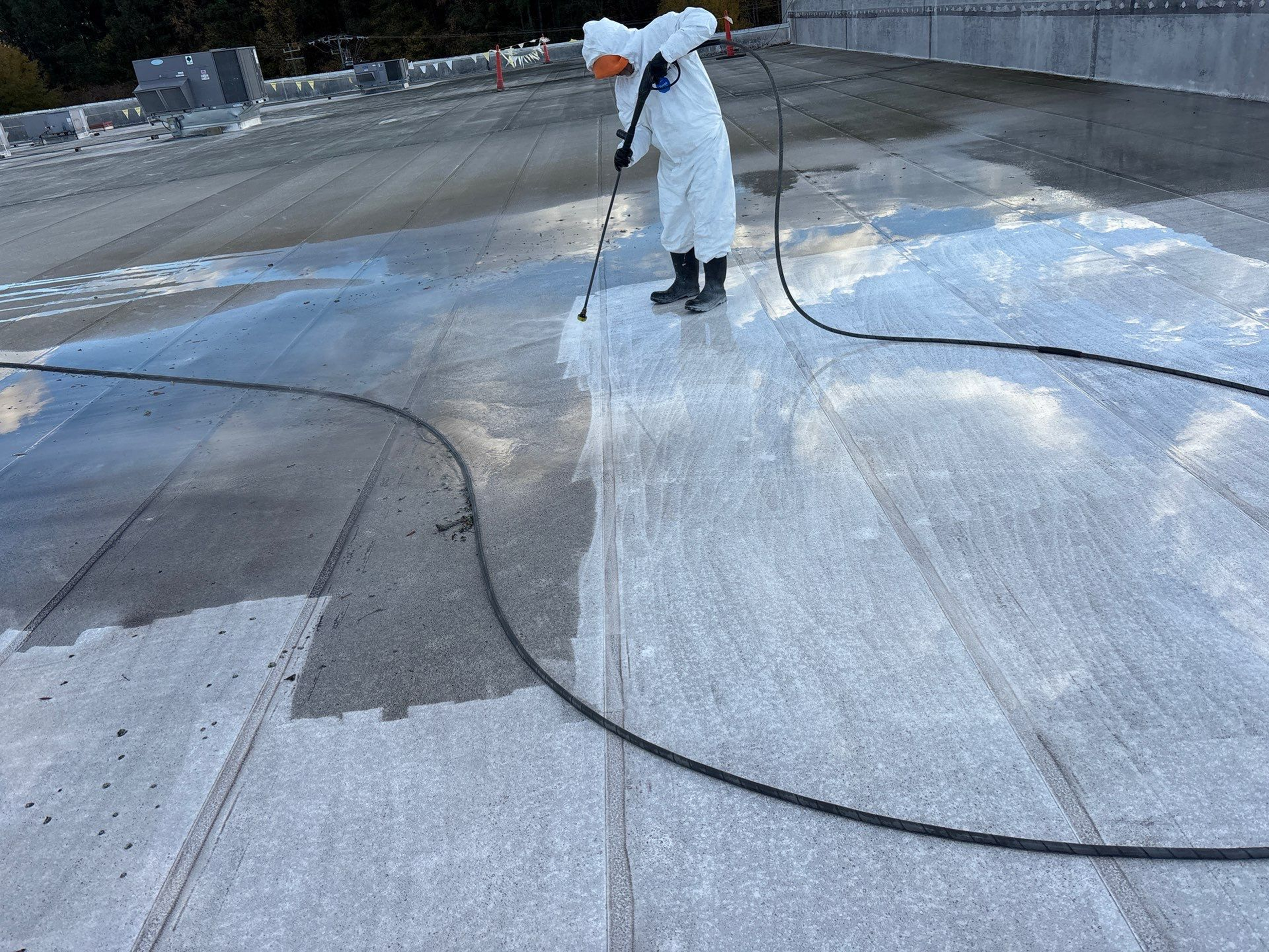 Person pressure washing a large concrete surface outdoors.