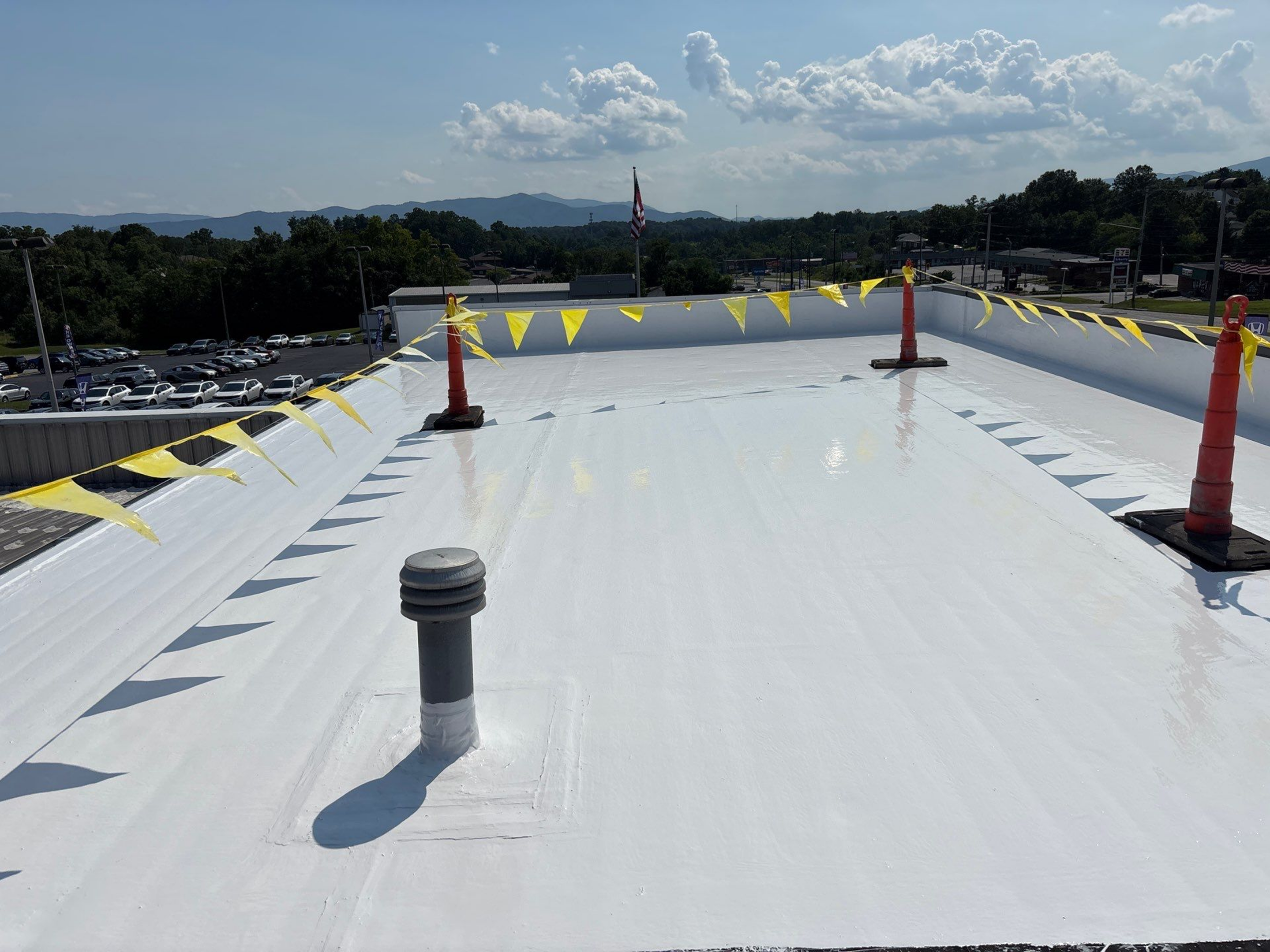 A clean, white rooftop with ventilation pipes and safety flags under a blue sky.